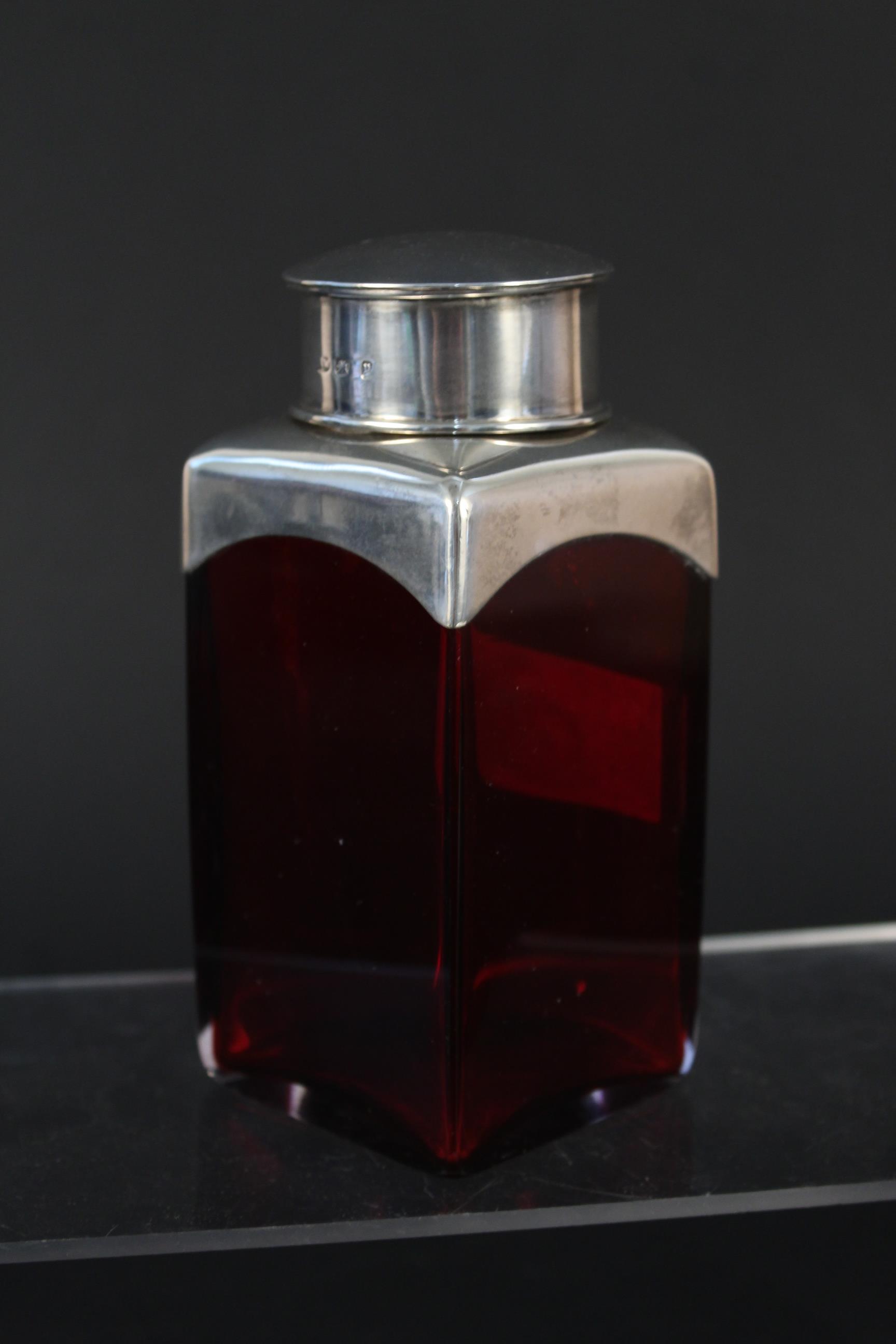 A silver lidded red glass bottle,