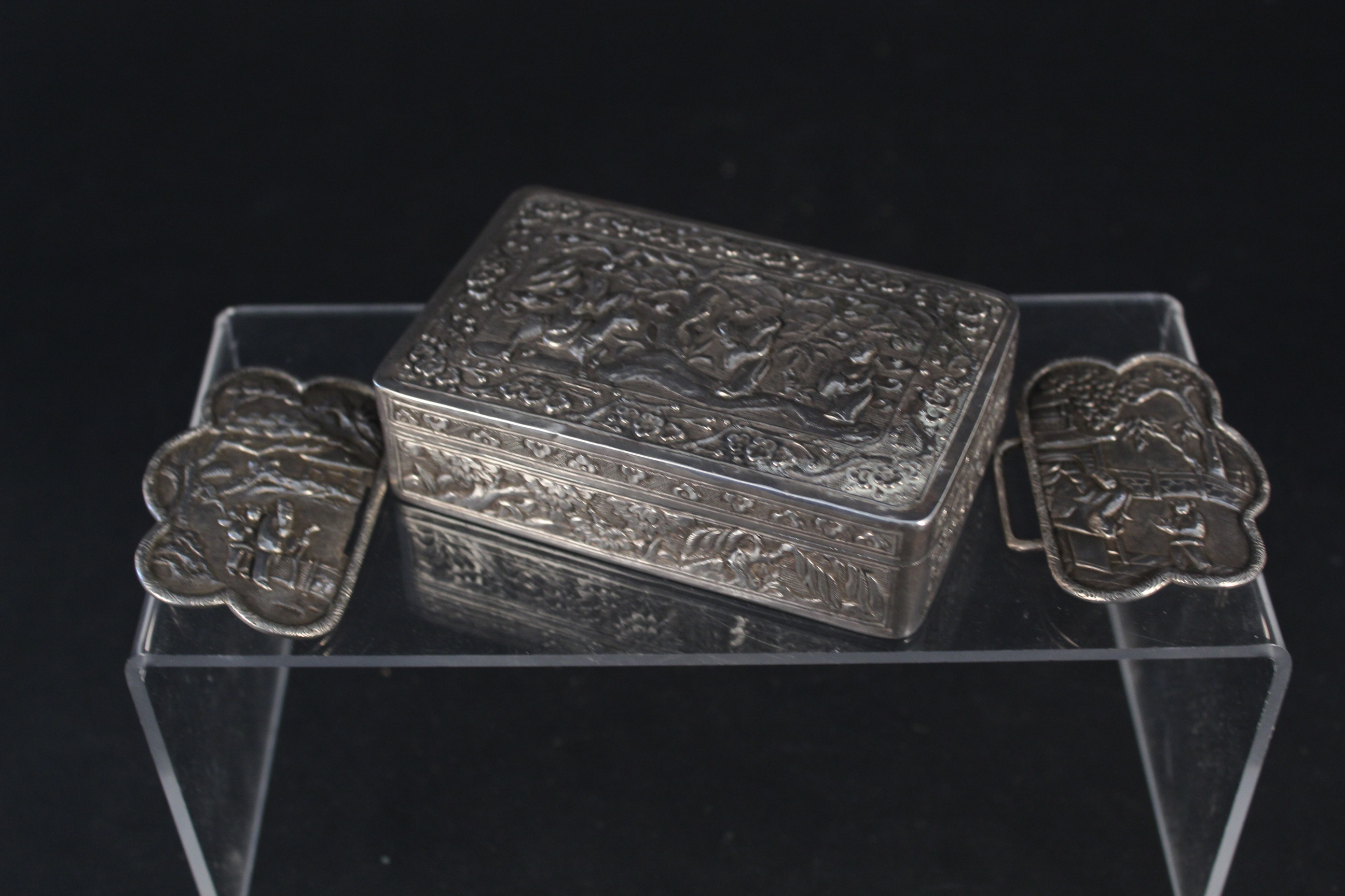 A white metal oriental style box embossed with figures and flora together with an incomplete white