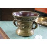 A heavy antique bronze mortar with script, band of scrolling ornamentation and twin dolphin handles,