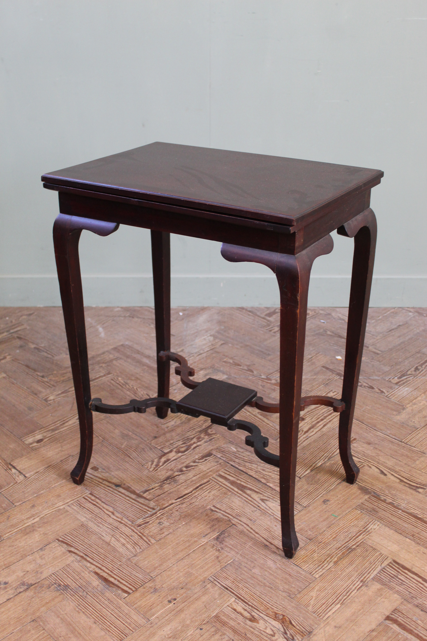 An Edwardian mahogany swivel top games table on cabriole legs and shaped under tier,