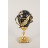 A 20th Century Russian Nephrite egg on gilded brass stand with brass ribbon and feather applied