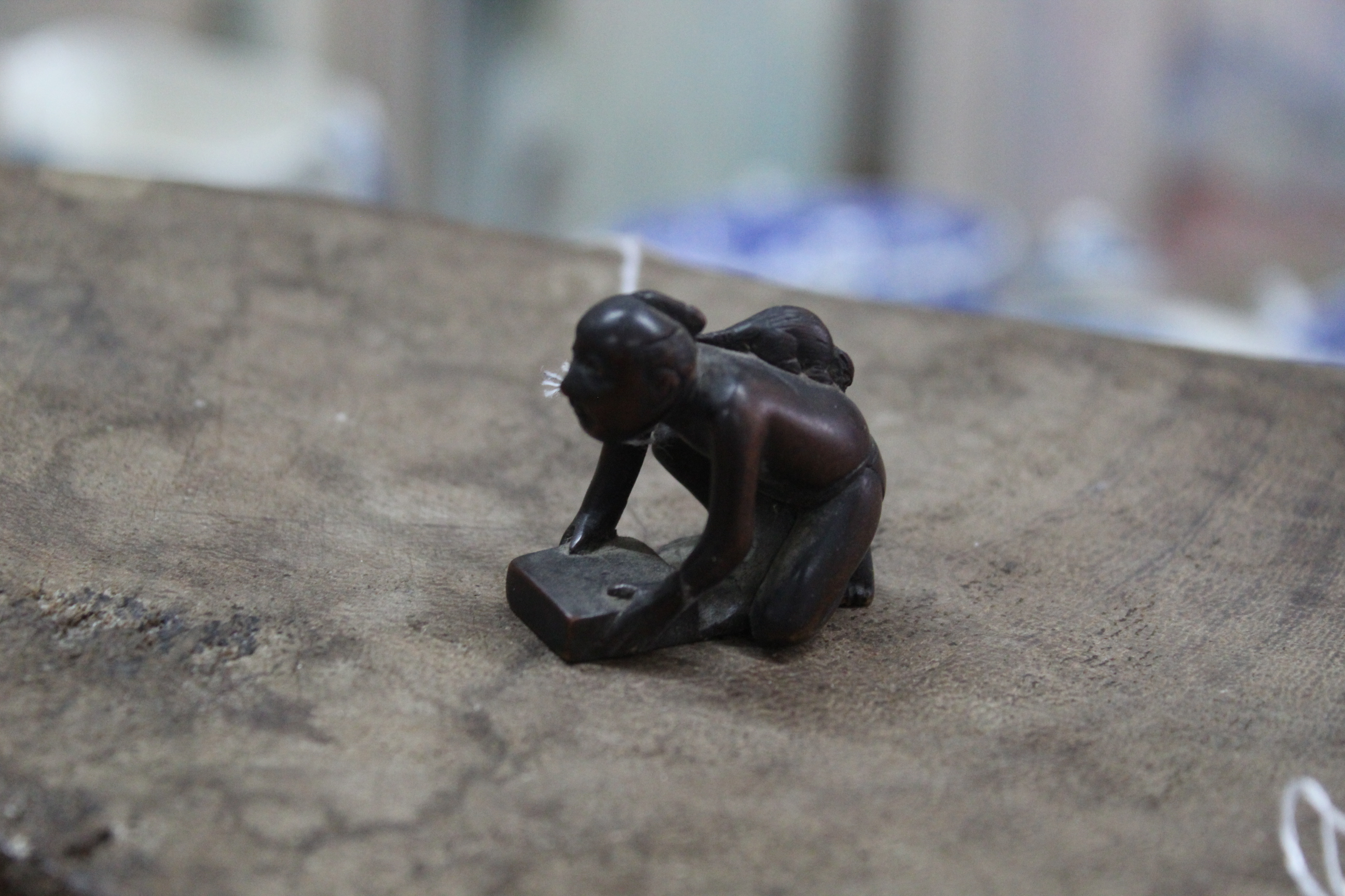 An antique carved wood netsuke of a kneeling figure of a man with a rat on his back,