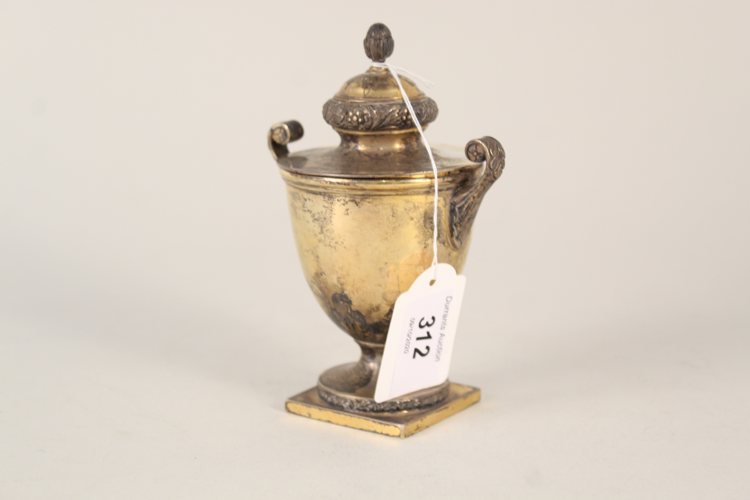 A silver gilt lidded urn with raised and etched decoration of acorn finials,