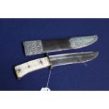 An Eastern 'Bowie style' knife with its white metal embellished sheath