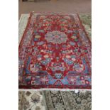 A Persian rug with a blue and floral border on a red ground,