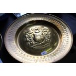 A large Arts and Crafts brass alms dish with central embossed Coat of Arms and punch decorated