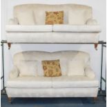 A pair of Edwardian style two seater sofas, upholstered in a floral pattern cream fabric, raised