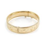 A 9ct gold bangle, with engraved foliate decoration, on a snap clasp with safety chain as fitted,
