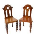 A pair of Victorian gothic mahogany hall chairs, the backs with open tracery, solid seat, raised