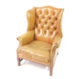 A Georgian style mahogany wing back club armchair, upholstered in button back tan leather, with