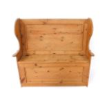 A pine settle, of traditional form, with wing arms and solid back, lift up seat and panelled