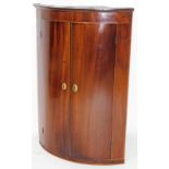 A George III mahogany hanging barrel corner cupboard, with elaborate oval escutcheons and fitted