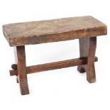 A rustic stool, of rectangular form, with heavy block top, on shaped legs joined by a block