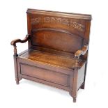 An oak settle, with a foliate scroll back, scrolling arms and box base with hinged seat, raised on