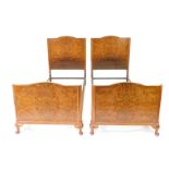 A pair of early 20thC walnut single beds, with shaped head and foot boards, iron frames and side