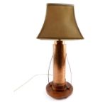 An Art Deco copper table lamp, of hammered double cylindrical form, with scroll arms, raised on a