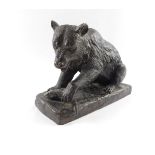 A bronze figure of a bear, modelled seated with it's front paw resting on a fish, raised on a