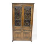 An Old Charm oak cupboard bookcase, with two glazed doors opening to reveal two shelves above a pair