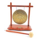 A Burmese brass table gong, in a wooden frame, on a serpentine base, with clanger, 25cm W.