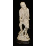 A Japanese Meiji period ivory okimono figure, of a man in robes holding fan, standing on a rocky