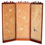 An early 20thC three fold screen, with heavily carved top, set with material panels, one with