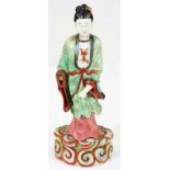 A Chinese porcelain figure of a standing lady, in flowing green and pink robes with black red and