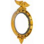 A Regency style port hole mirror surmounted by an eagle, the circular domed glass in a carved case r