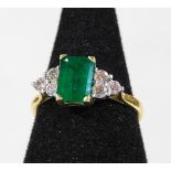 An 18ct gold emerald and diamond dress ring, with rectangular cut emerald, in four claw setting, mea