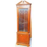 A mahogany finish corner display cabinet, with broken pedimented top and urn finial.