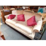 A two seater sofa with scroll arms and loose cushions, upholstered in a cream fabric, raised on