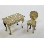 A Continental early 20thC miniature silver repousse table and chair, decorated with cherubs and