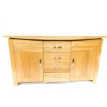 A light oak sideboard, fitted with four central drawers, flanked by two cupboards with tongue and