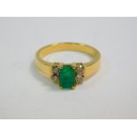 An emerald ring, flanked by two pairs of diamonds in a stepped shank, yellow metal stamped 18K,