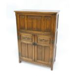 An Old Charm oak drinks cabinet, with cantilever fall front and top, with linen fold panels, the