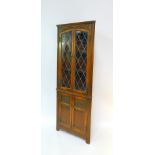 An Old Charm oak corner cabinet, the slightly outswept pediment over two glazed doors opening to