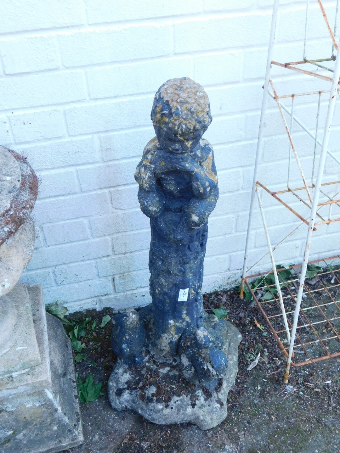 A reconstituted stone figure of a boy, atop a column flanked by a rabbit and a squirrel.