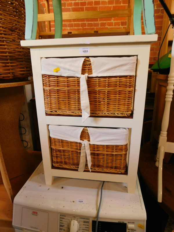 A white painted wooden bedside chest, with two shelves, containing linen lined wicker baskets,