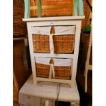 A white painted wooden bedside chest, with two shelves, containing linen lined wicker baskets,