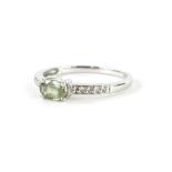 A 9ct white gold solitaire ring, claw set with green stone, flanked by small white stones to each