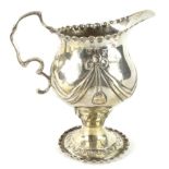 A George III silver cream jug, the helmet shaped body raised with garlands and flowers and