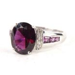 A 9ct white gold dress ring, claw set with an oval purple stone and flanked by small white and