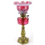 A late Victorian cranberry and brass oil lamp, with shaped floral milk glass shade, set with flowers