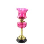 A Victorian brass oil lamp, with cranberry tinted shade and reservoir on reeded column with