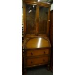 A mid 20thC oak bureau bookcase, with lead glass sunburst door, carved fall and two drawers, on