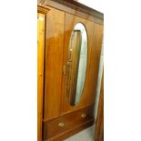 A late Victorian mahogany and boxwood strung wardrobe, with oval mirrored door above drawer beneath,