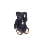 A Merrythought plush jointed Penny Black teddy bear, in black, with faux stamp to the ribbon,