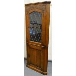 An Old Charm style oak corner cupboard, with lead glass panel door, flanked by carved fluting