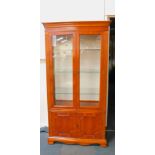 A yew wood display cabinet, the outswept pediment over two glazed doors, opening to reveal three