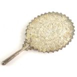 An eastern silver coloured metal hand mirror, embossed with flowers, leaves, etc., and with a jagged