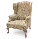 A mahogany wingback chair in George III style, upholstered in figural tapestry fabric on cabriole